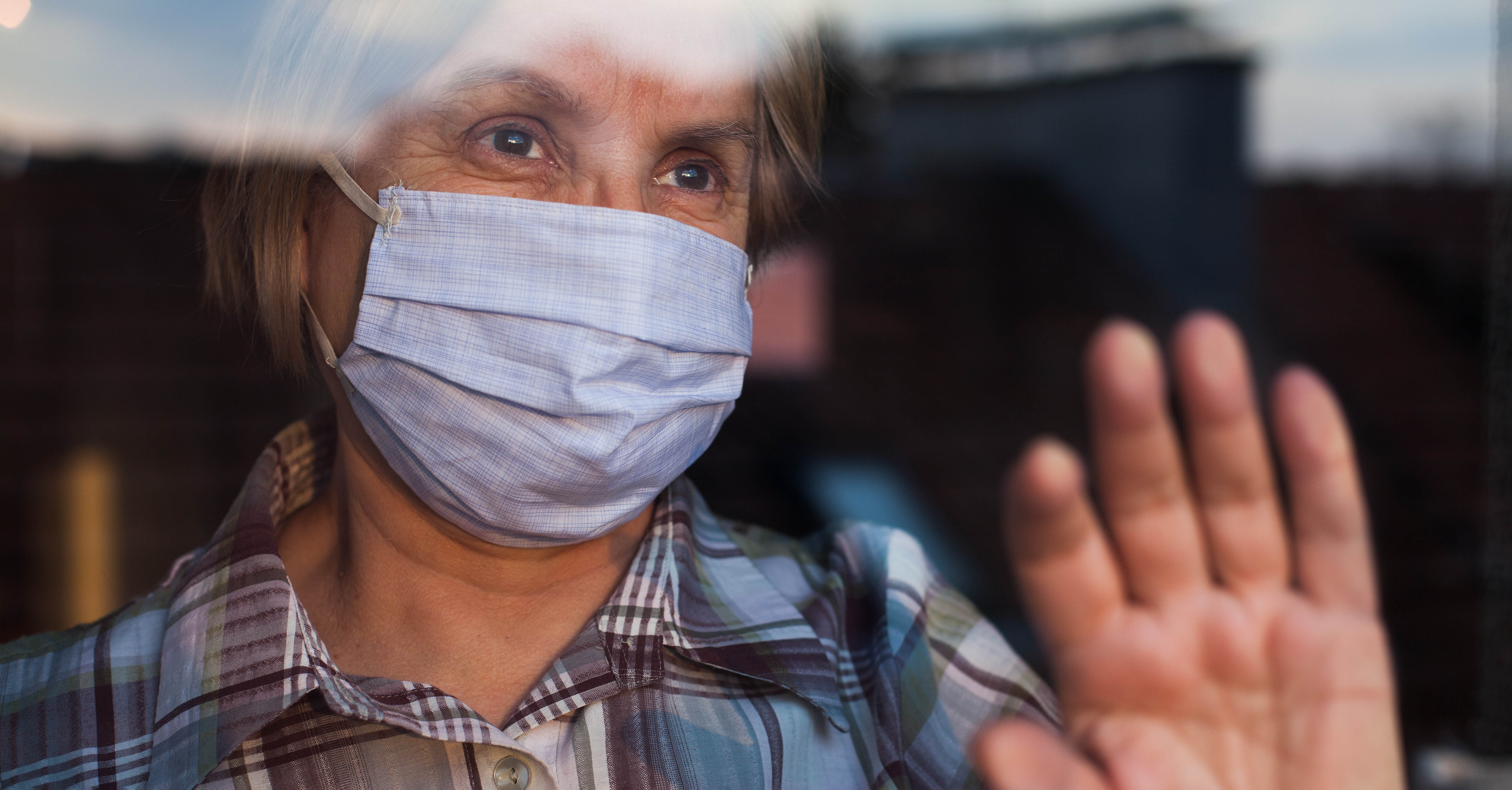 An older adult wearing a face mask and looking out of a window.