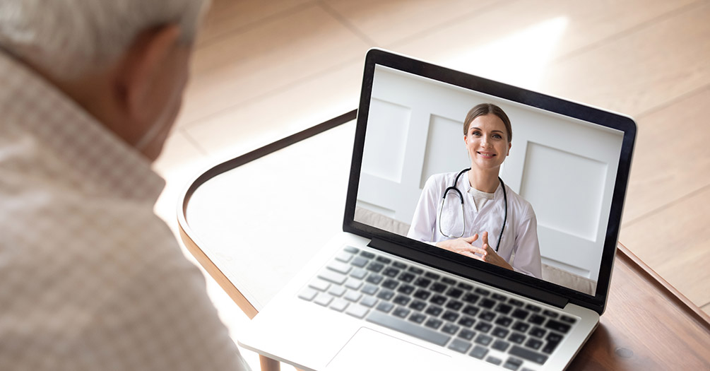 A doctor conducting a telehealth meeting with an elderly male patient.