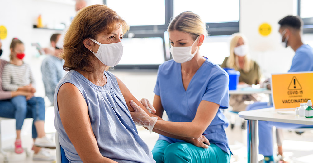 An older woman receiving a COVID-19 vaccine from a nurse. 