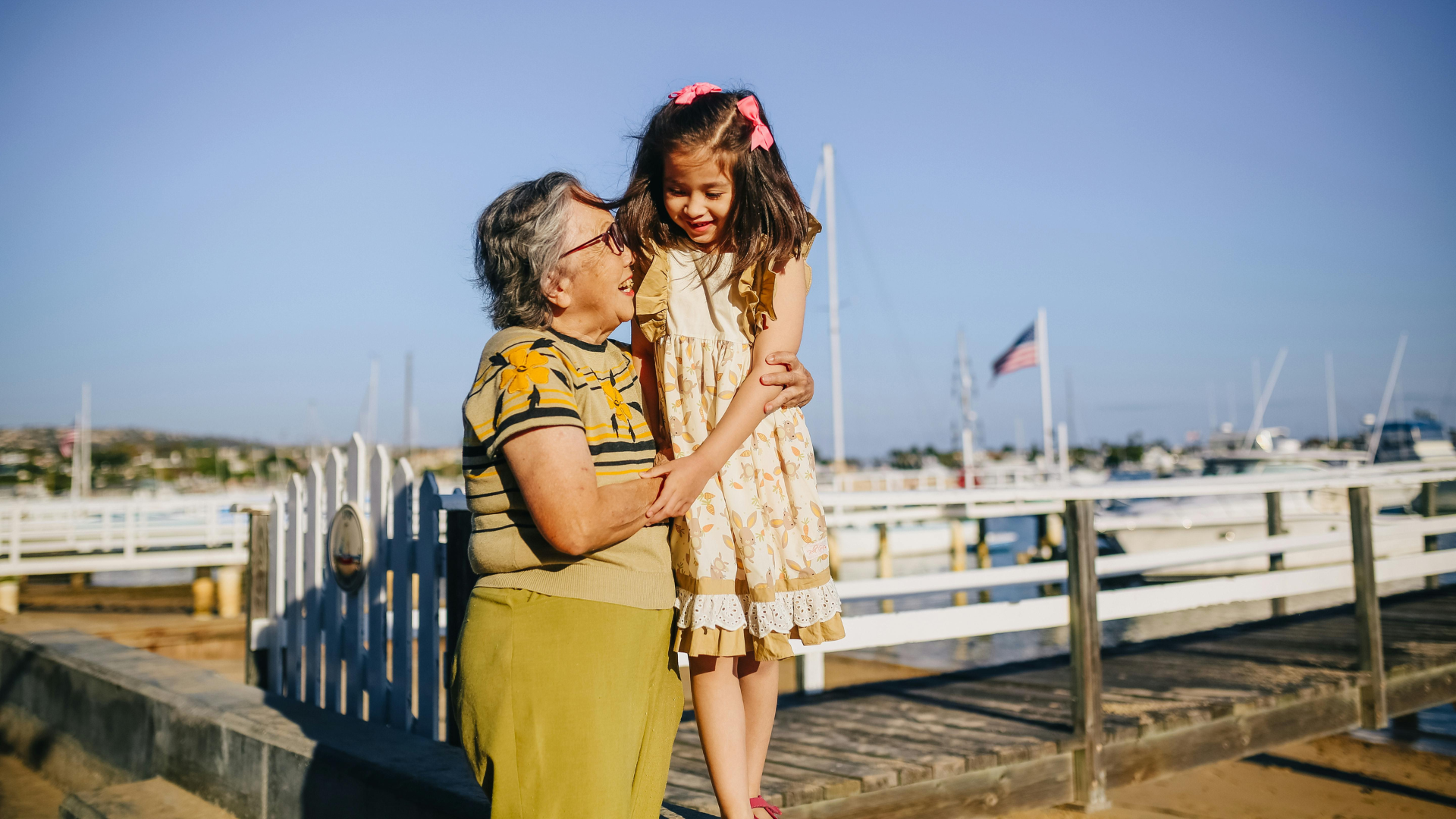 A grandmother and granddaughter smile together on a pier.