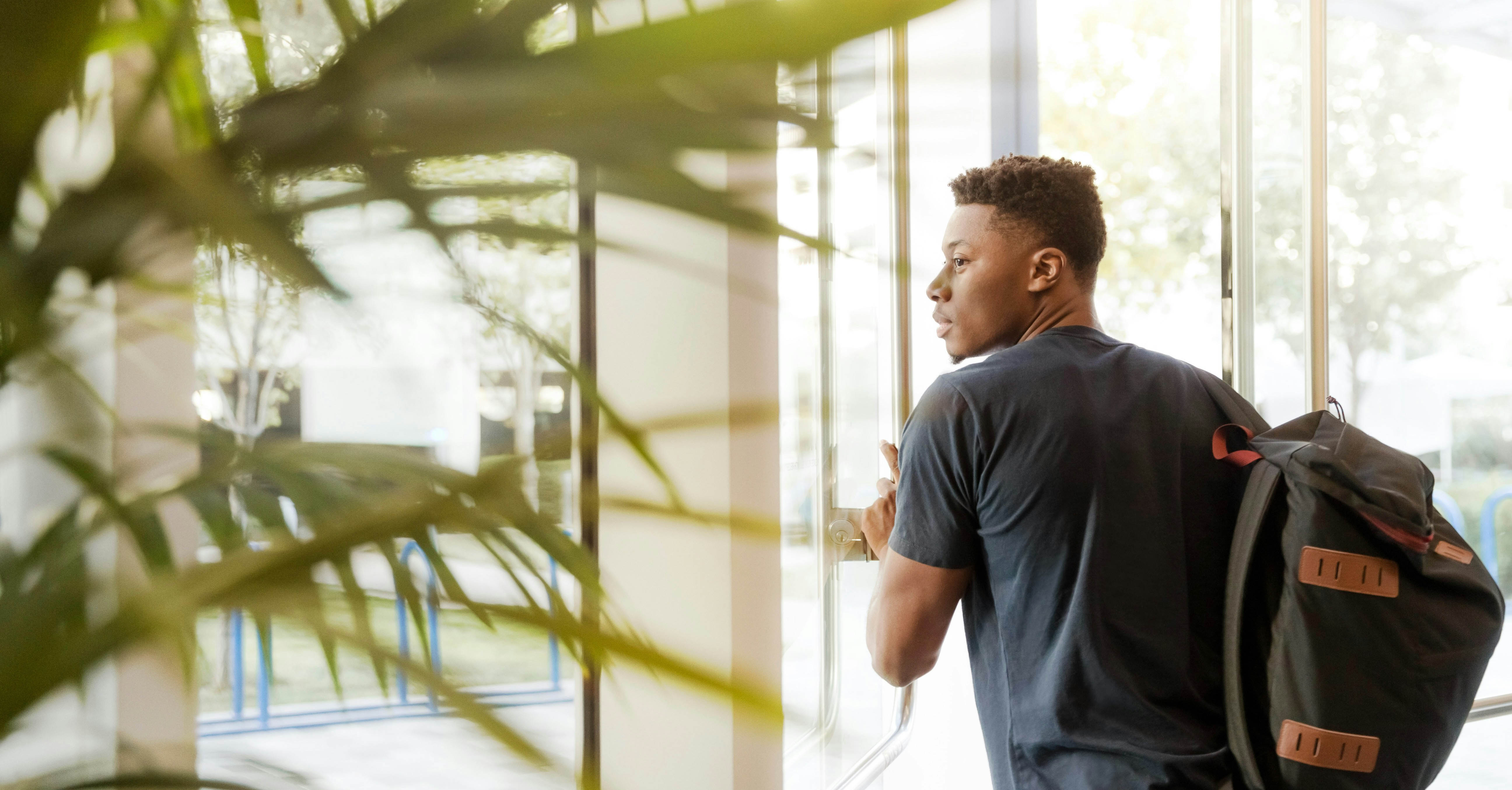 A male student opening a glass door into a building.