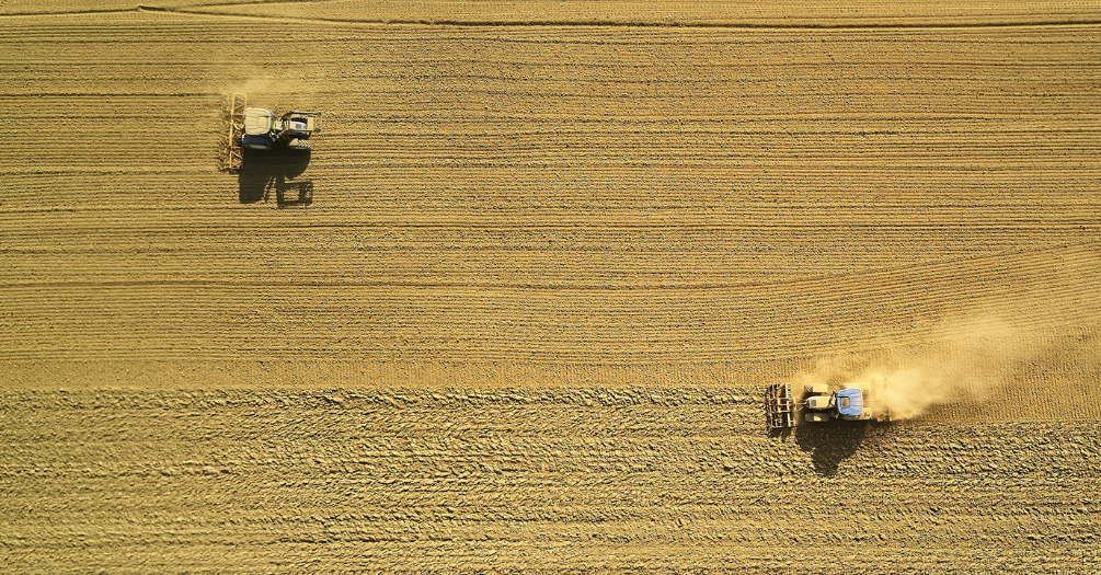 Farming vehicles stirring up dust on an arid farm